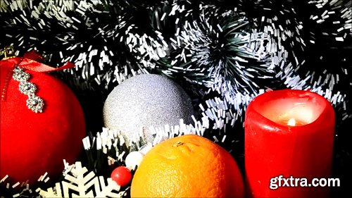 Cristmas toy, tangerine and burning candle on background of pine-needles