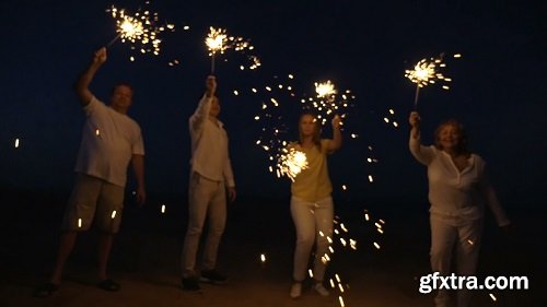 Slow motion steadicam shot of friends or family with firework sparklers on the beach at night celebration time