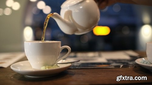 Close up shot of female hand pouring black hot tea from the pot into the cup