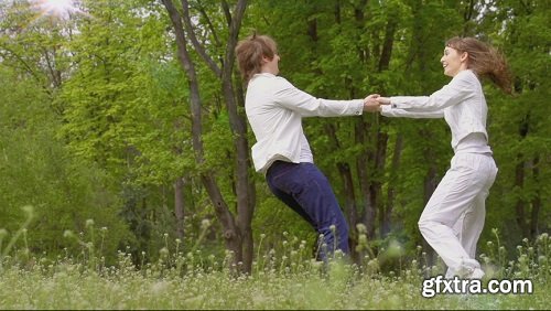 Young man and woman are spinning in the center in spring park background slow motion filmed