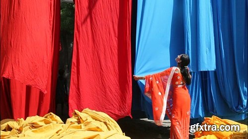 Woman in saree checking the quality of freshly dyed fabric hanging from bam