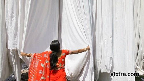 Woman in saree checking the quality of freshly dyed fabric hanging from bam