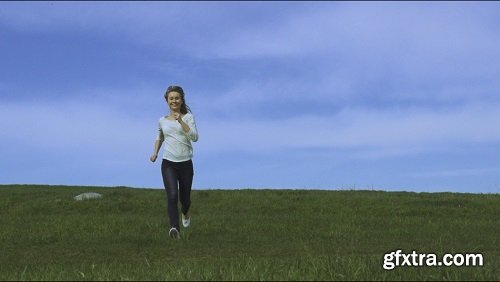 Young happy woman is running and jumping by the camera blue sky and green grass on the background