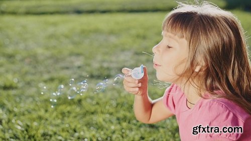 Cute little girl is blowing soap bubbles in the garden outdoors on a sunny day slow motion 240 fps