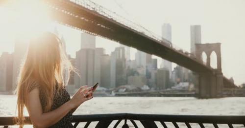 Beautiful Girl with Long Hair in Sunglasses Using Smartphone App at Sunset River Quay Near Brooklyn - VZ3JR75