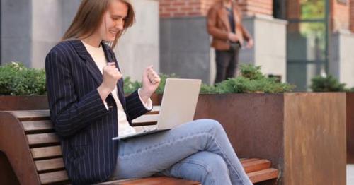 Excited Woman Celebrating Success on Laptop Sitting on Bench - 279V5EN