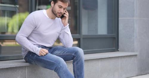 Handsome Man Talking on Phone while Sitting Outside Office - M4KHGQV