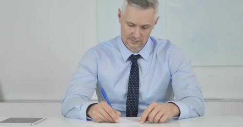 Senior Businessman Writing Letter at Work, Paperwork - 8E9ZLTA