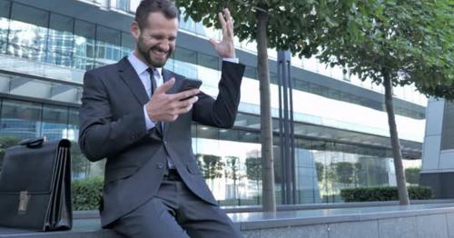 Beard Businessman Excited for Success while Using Smartphone - LX8H76R