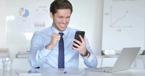 Young Businessman Celebrating Success on Smartphone - 6XQYR2T