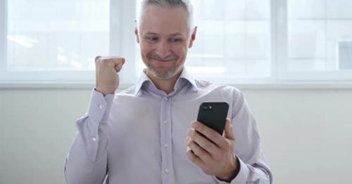 Middle Aged Man Excited for Success while Using Smartphone - JRT37UC