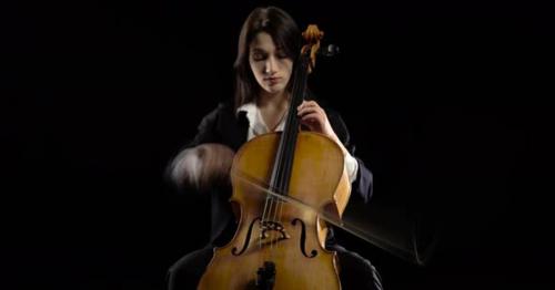 Musician in a Dark Room Sits and Plays a Violoncello Rehearsing a Composition. Black Background - CP9Y7S4