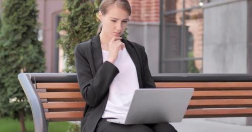 Pensive Young Businesswoman working on Laptop, Sitting Outdoor on Bench - HGYA7P6