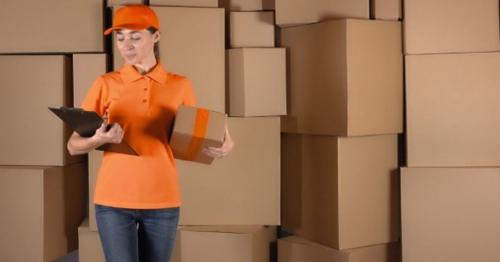 Pretty Female Courier in Orange Uniform Delivering a Parcel - 87CYEJD