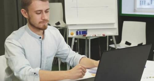 Attractive Young Man Using His Smart Phone and Laptop at the Office - 2V6NRCM