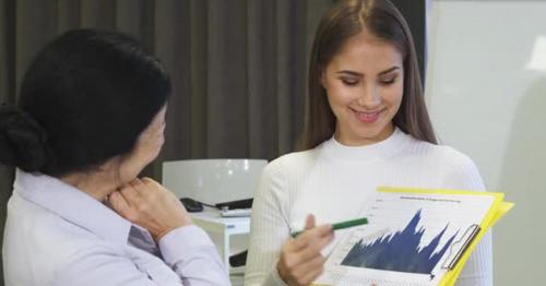 Beautiful Young Businesswoman Showing Diagrams To Her Senior Colleague - LY56VDZ