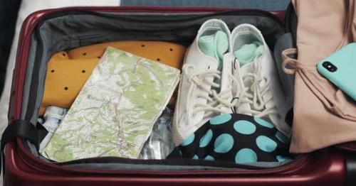 Woman's Hands Packing Suitcase for a Journey on the Bed at Home - M65GZ9V