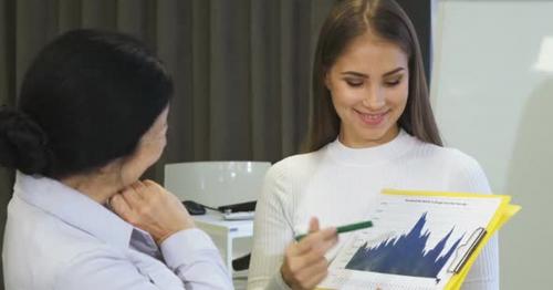 Young Businesswoman Showing Diagrams To Her Senior Colleague - WHKYRPM