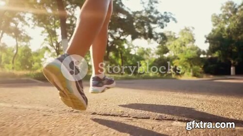 Videoblocks - Girl runs through the park in the morning. Sporty young attractive brunette woman running on empty road in the morning. Slow motion. Only legs 