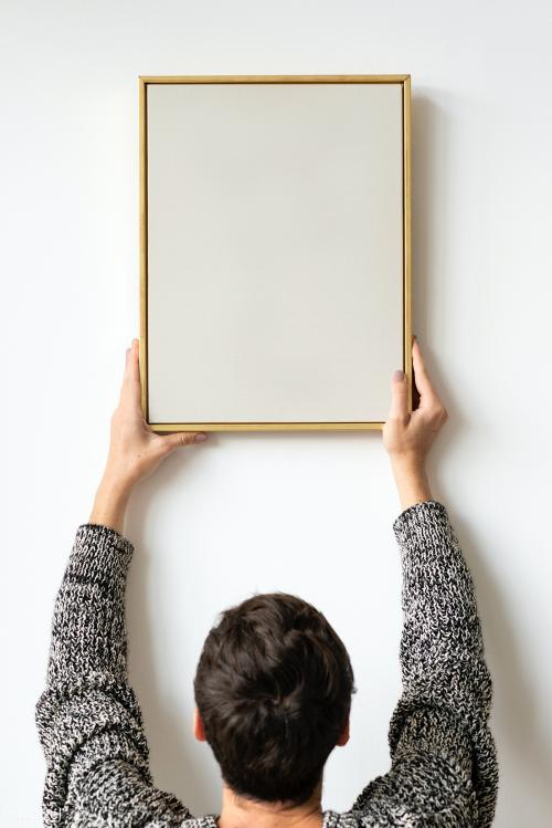 Woman in a black sweater hanging a wooden frame on a white wall mockup - 1231717