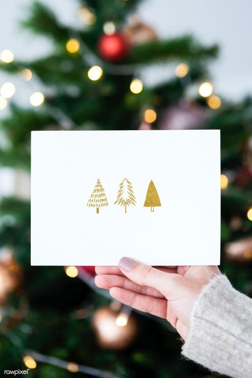 Woman holding a Christmas card in front of a Christmas tree mockup - 1231770