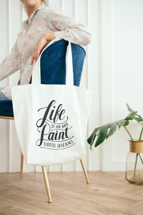 White tote bag mockup hanging on a blue velvet chair - 1210152