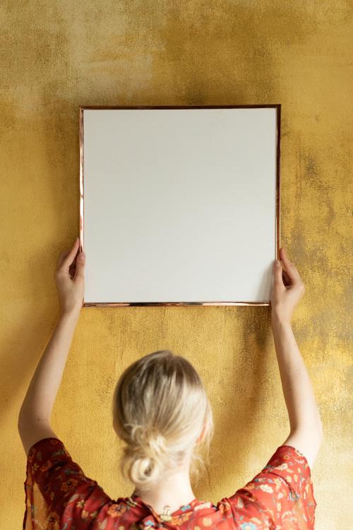 Woman hanging a frame mockup on a grunge yellow wall - 1212438