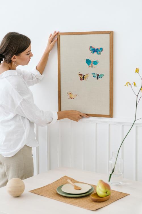 Woman hanging a photo frame on a white wall - 1215239