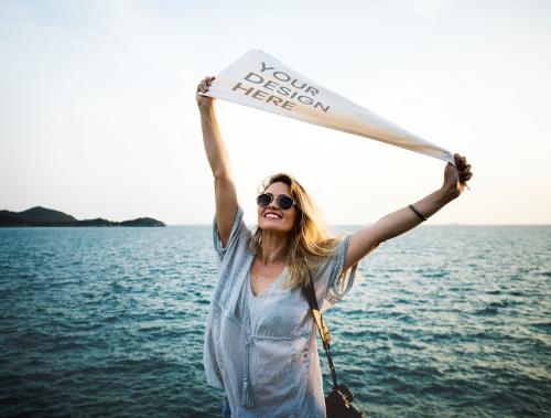 Woman holding a white cloth mockup by the sea - 894837