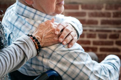 Elderly man on a wheelchair holding his wife hand on his shoulder - 2027135