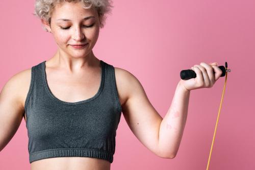 Young active girl with a skipping rope for cardio workout in a pink background studio - 2210603