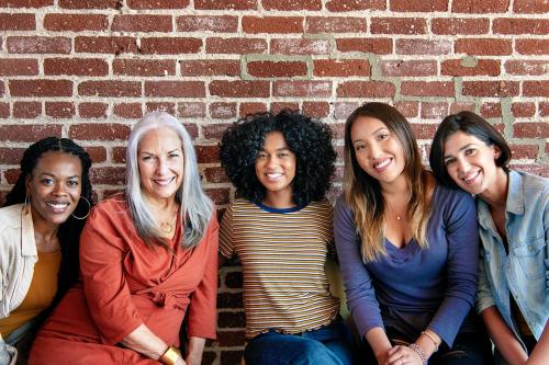 Diverse women sitting together by a brick wall - 2027377