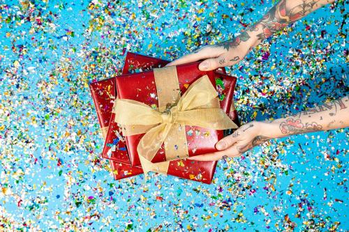 Tattooed hand holding red gift boxes with confetti - 2052084