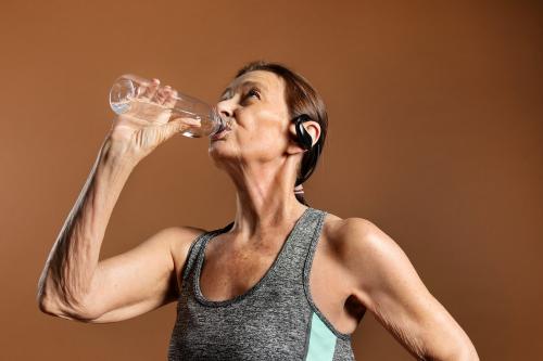 Thirsty senior woman in an active sportswear drinking water on a brown wall - 2223244