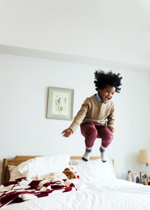 Young happy kid having fun jumping up and down on a bed - 2024982