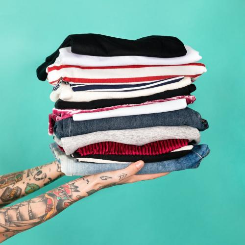 Hands with tattooed holding stack of folded clothes - 2053206