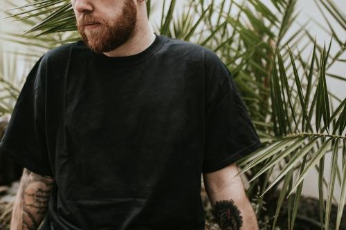 Tattooed man standing by the palm leaves - 2273329