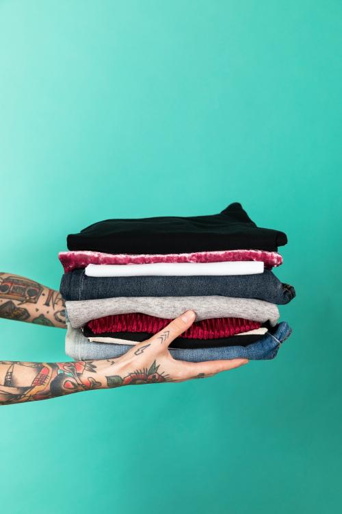 Tattooed hands holding a stack of folded clothes - 2053205