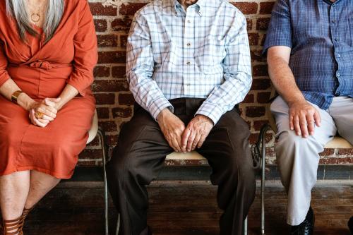 Diverse elderly people sitting in a row against a brick wall background - 2027412