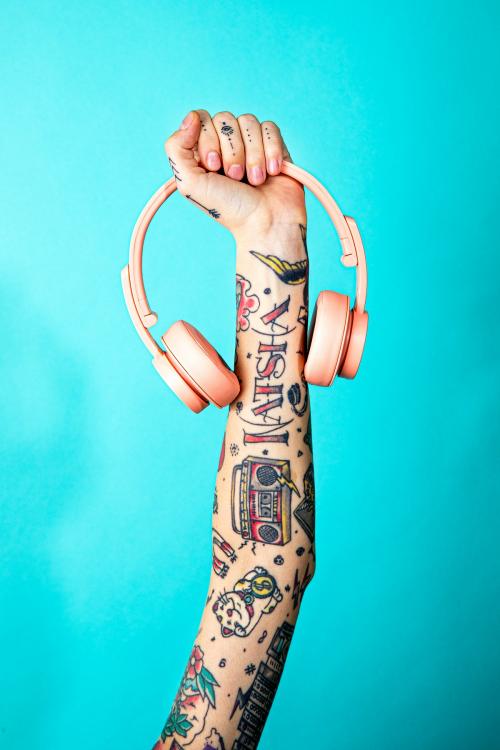 Tattooed arm holding a pink headphones - 2056059