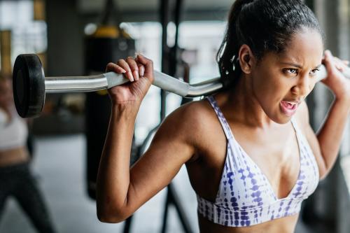 Woman exercising weighlifting with barbell at fitness gym - 2107307