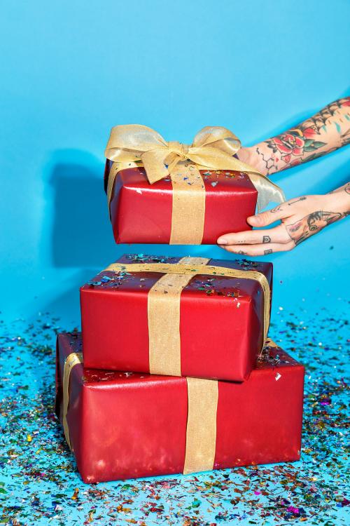 Tattooed hand holding red gift boxes with confetti - 2053898