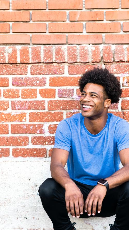 Cheerful man sitting by a brick wall - 2041668