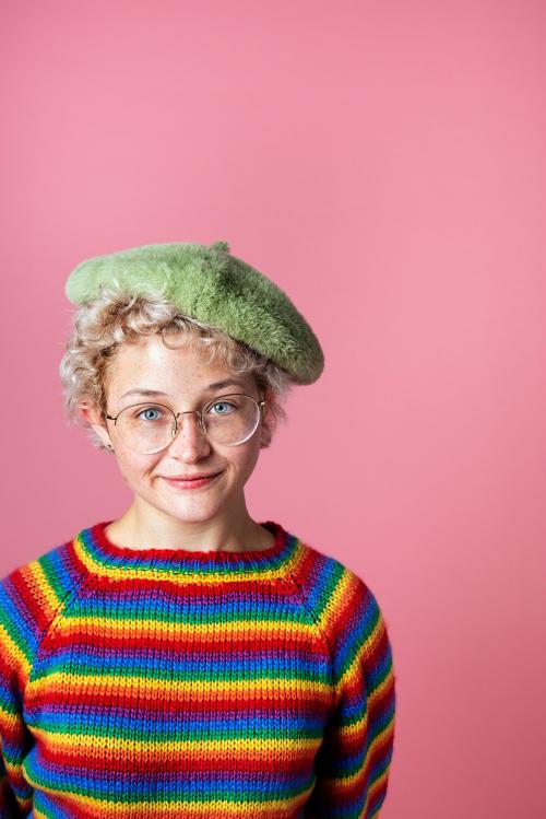 Cheerful girl wearing rainbow sweater and green beret in a pink background - 2223245