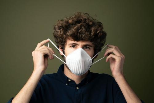 Young Caucasian man putting on a disposable protective mask - 2223217