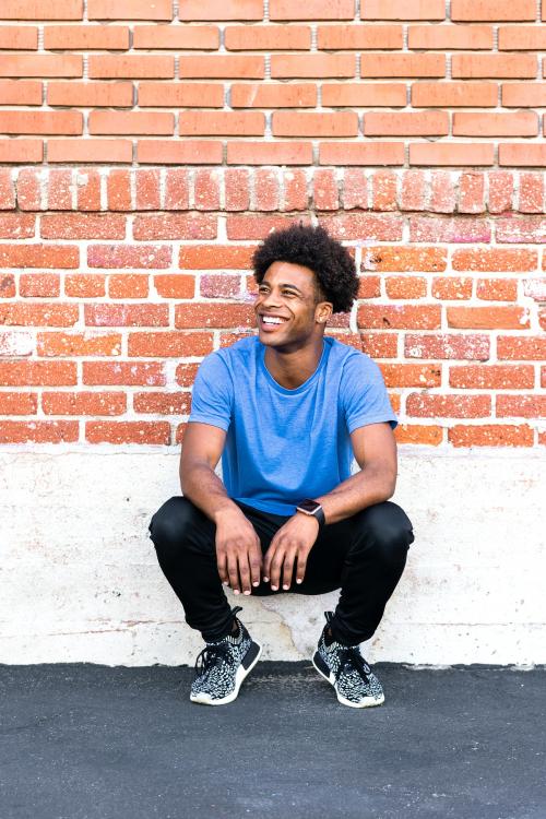 Cheerful man sitting by a brick wall - 2046423