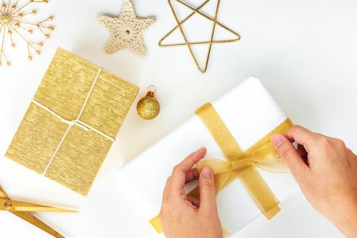 Woman tying a gold ribbon to a white present - 1231812