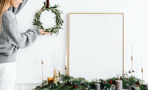 Woman hanging a Christmas wreath next to a blank white frame - 1231821