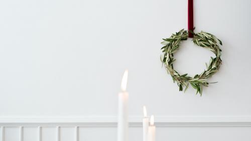 Christmas wreath on a white wall with lighted white pillar candles - 1231408