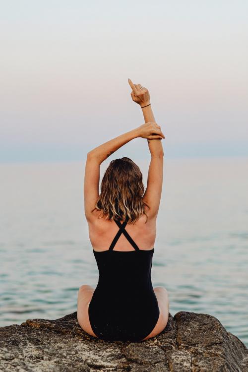 Rear view of a girl sitting on a rock at the beach - 1228340